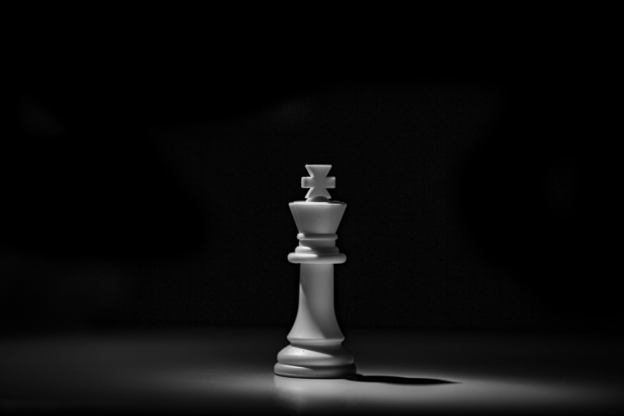 A white chess king piece lit against a black background